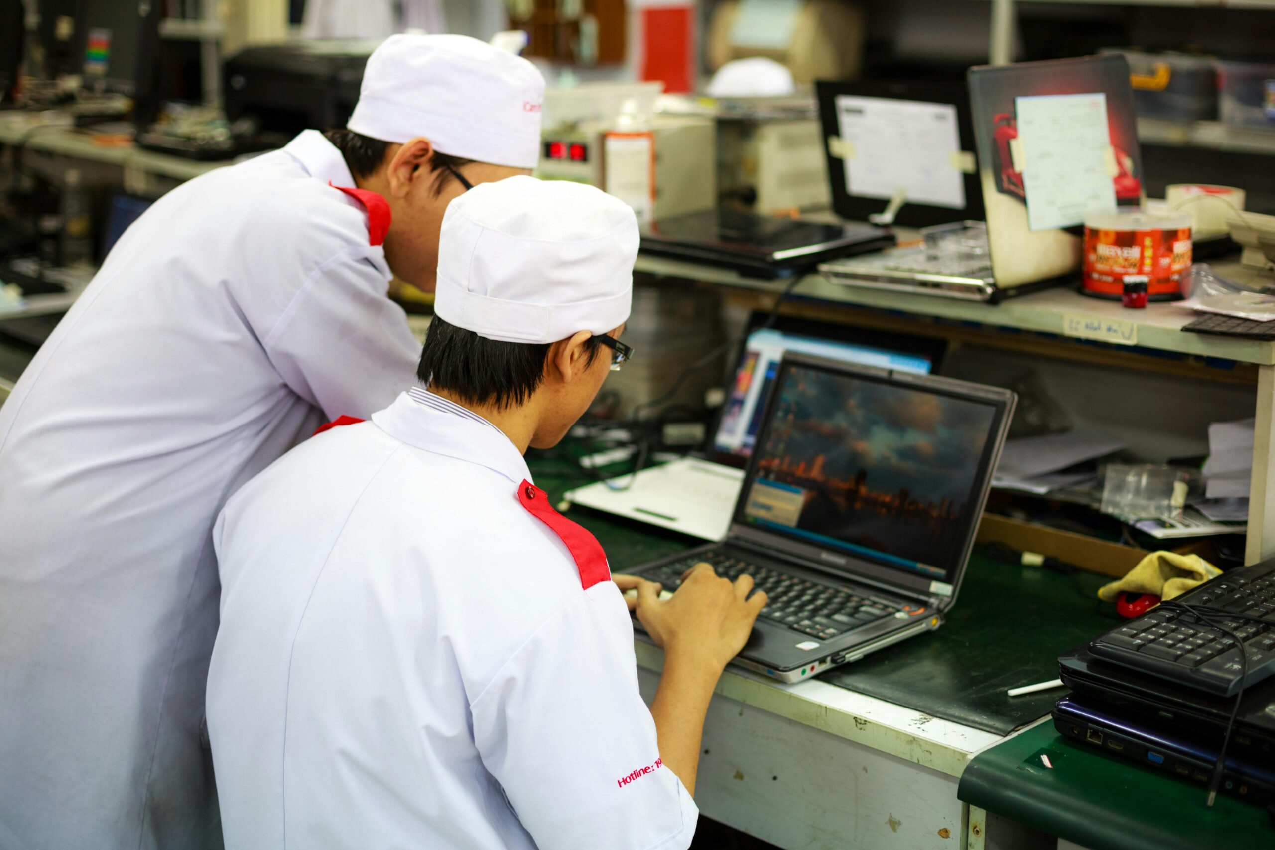 Two technicians in uniforms working on laptops in a laboratory setting. Focus on teamwork and technology.